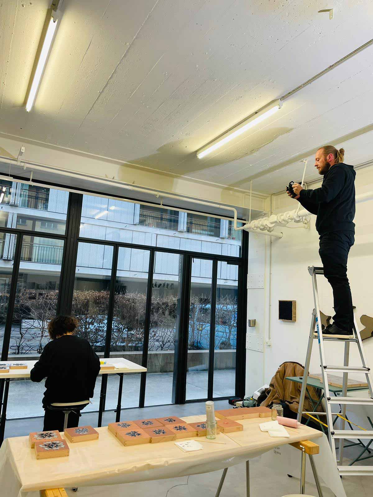 Videoproduzent auf einer Leiter filmt Künstlerin in ihrem Atelier